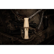 A close-up of a light-colored Power Calls Beau Brooks Signature Series Duck Call with a metallic band, set among darker duck calls and braided lanyards on a camo-patterned background.
